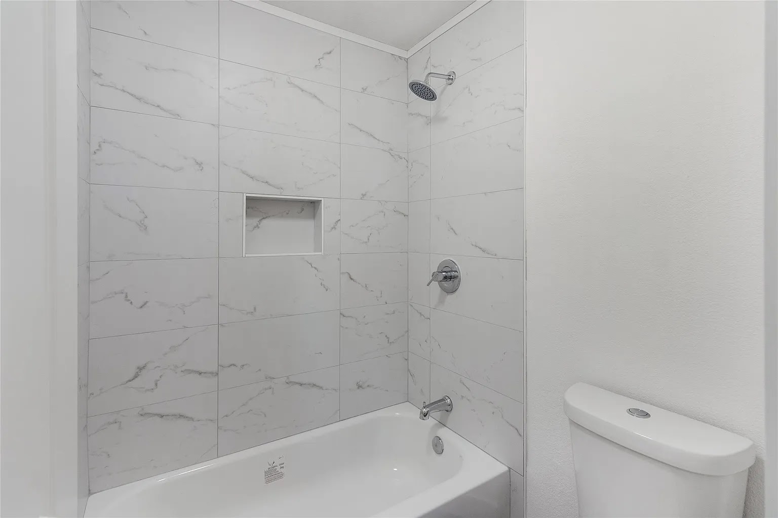 Freshly remodeled bathroom showing chrome shower head, marble tile surround, white soaking tub, and chrome fixtures in a DFW home